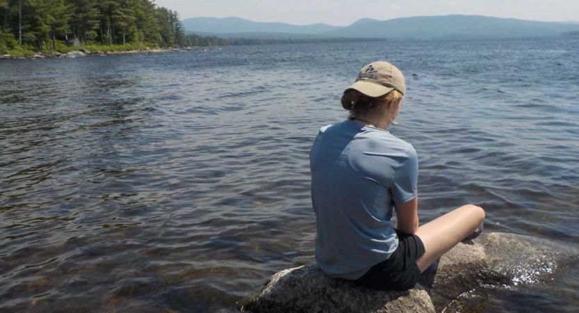 A person sits on a rock near a body of water